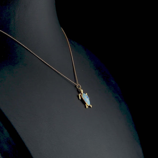 Özel tasarım altın kolye, kaplumbağa figürlü detaylarıyla ön planda; mavi mine işçiliği ve altın parlaklığı bir araya gelerek doğadan ilham alan zarif bir takı görüntüsü sunuyor.

