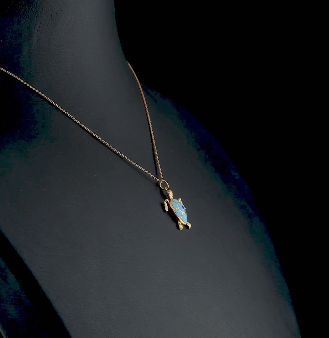 Özel tasarım altın kolye, kaplumbağa figürlü detaylarıyla ön planda; mavi mine işçiliği ve altın parlaklığı bir araya gelerek doğadan ilham alan zarif bir takı görüntüsü sunuyor.

